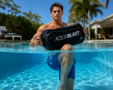 Fit athletic man lifting AquaBLAST bag out of pool in a tropical background